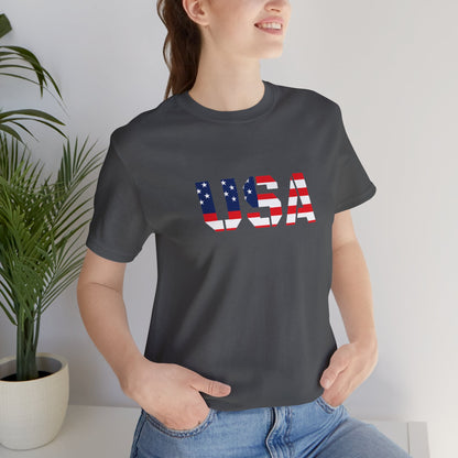USA flag text T-shirt by Printify featuring patriotic Fourth of July design, white cotton tee with red, white, and blue flag graphic.
