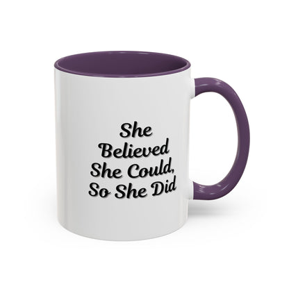 White ceramic motivational coffee mug with black text "She Believed She Could, So She Did" by Printify, shown on a wooden surface.