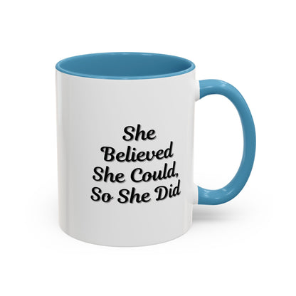 White ceramic motivational coffee mug with black text saying "She Believed She Could, So She Did" on the front.